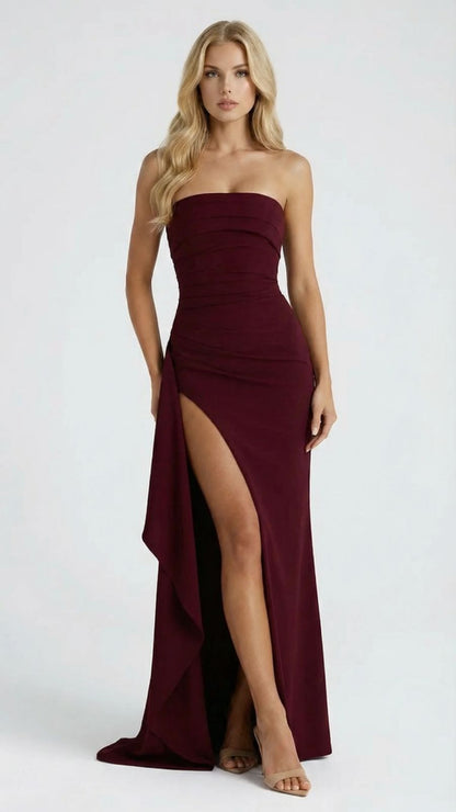 Women's burgundy ruched strapless maxi dress with a high thigh slit and cascading drape, front view.