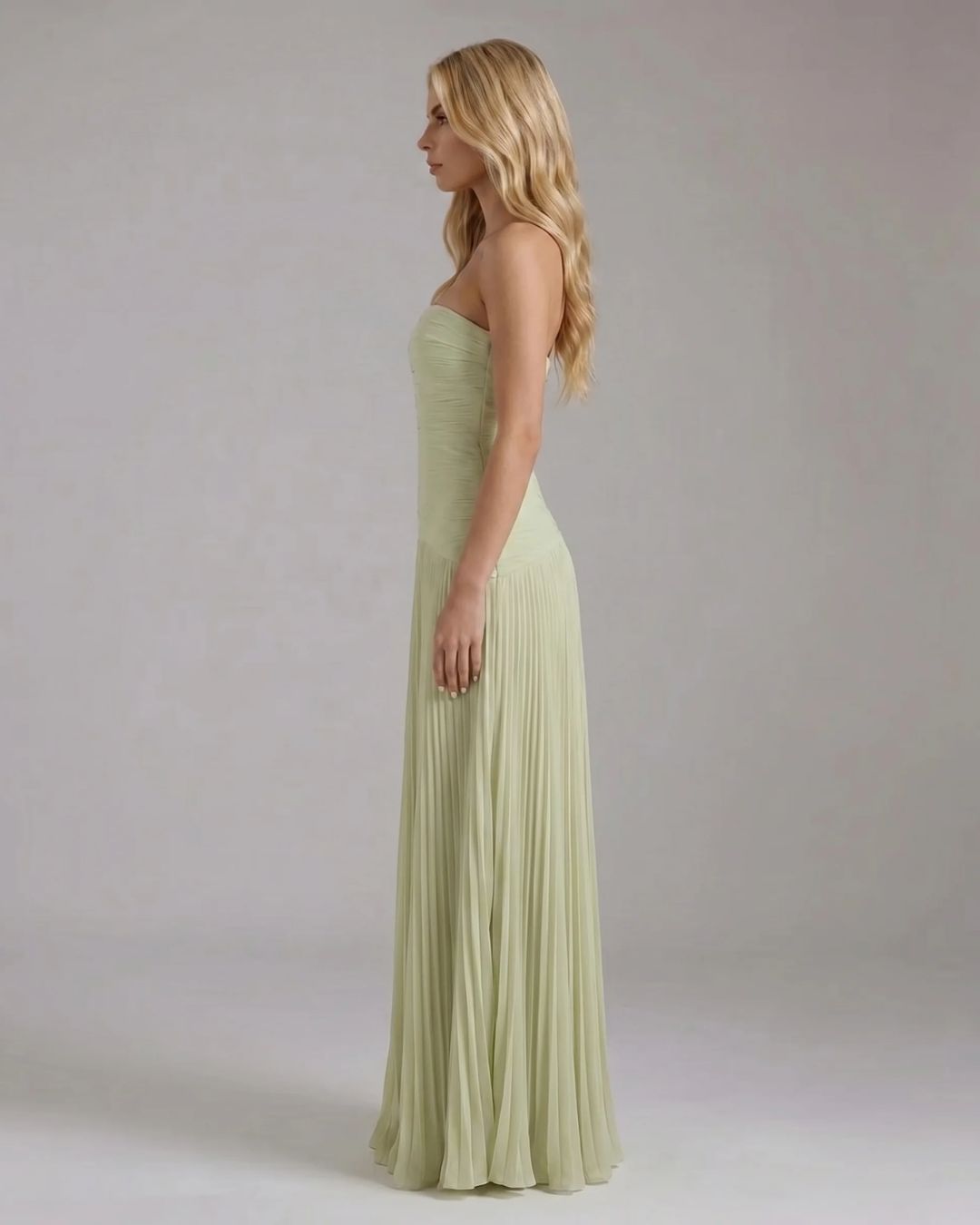 Side profile of the light green Kenzie Forest maxi dress, highlighting the fitted strapless bodice and vertical pleats.