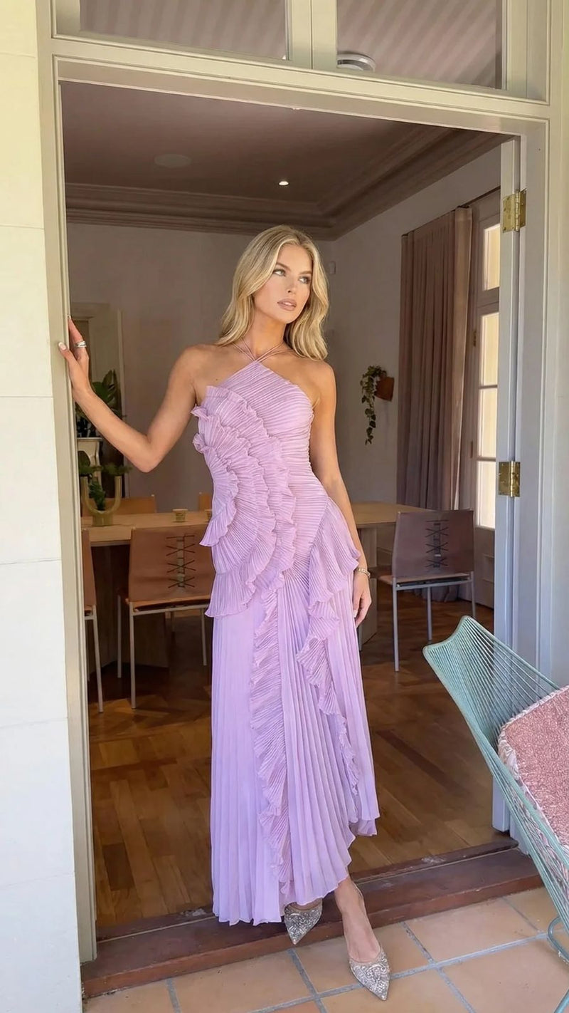 Elegant lavender Nathalie ruffle maxi dress with one-shoulder pleated bodice and flowing skirt, worn by a blonde woman in a doorway.