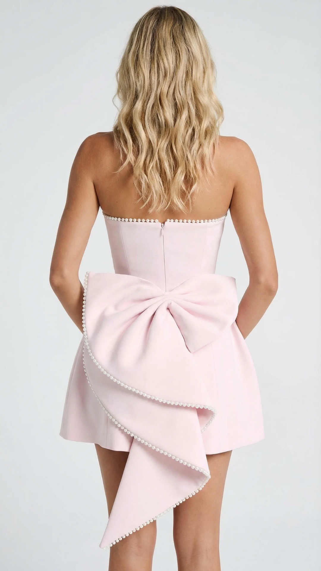 Back view of women's pink strapless mini dress featuring a large pearl-edged bow and a back zipper closure.