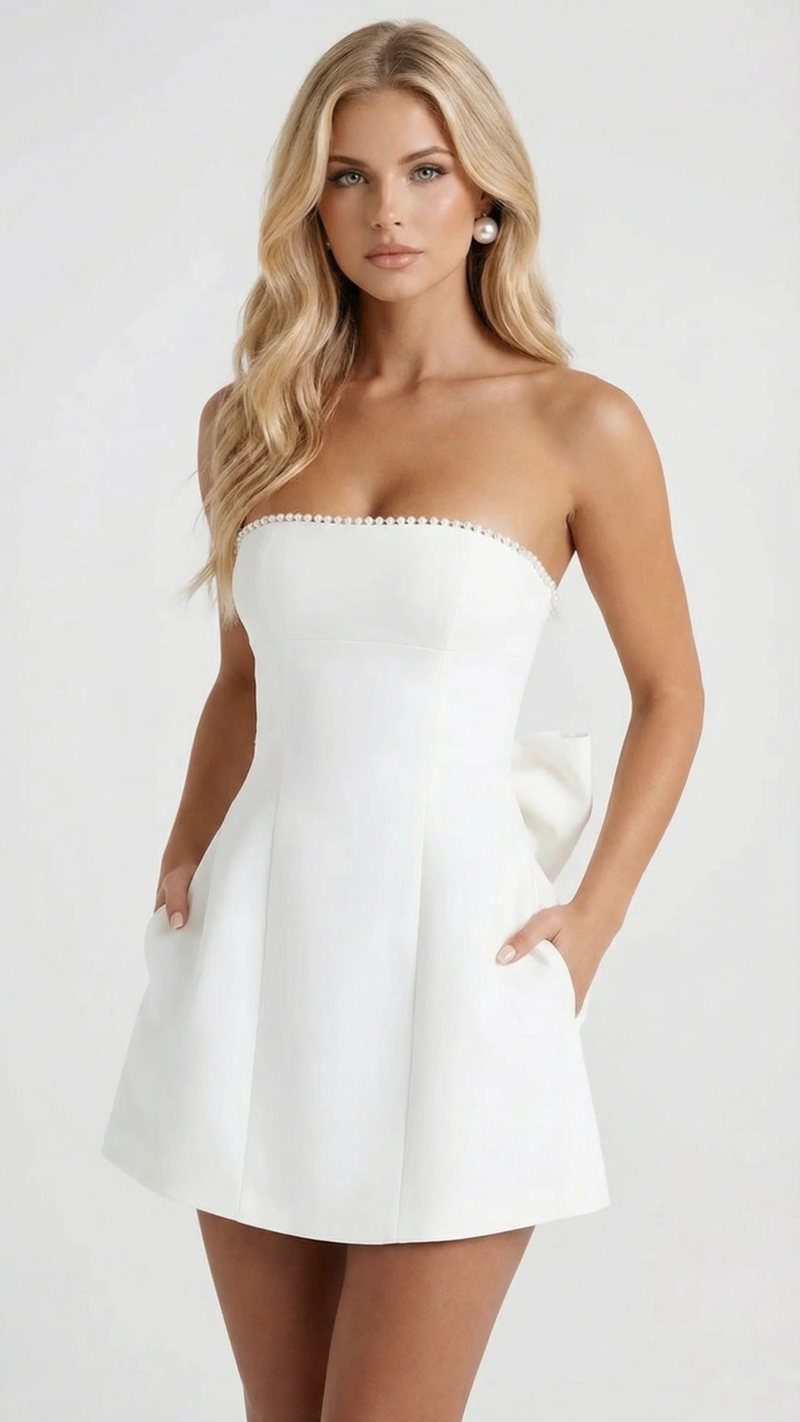 Side view of a white strapless mini dress with pearl trim, showing pockets and a small bow at the back.
